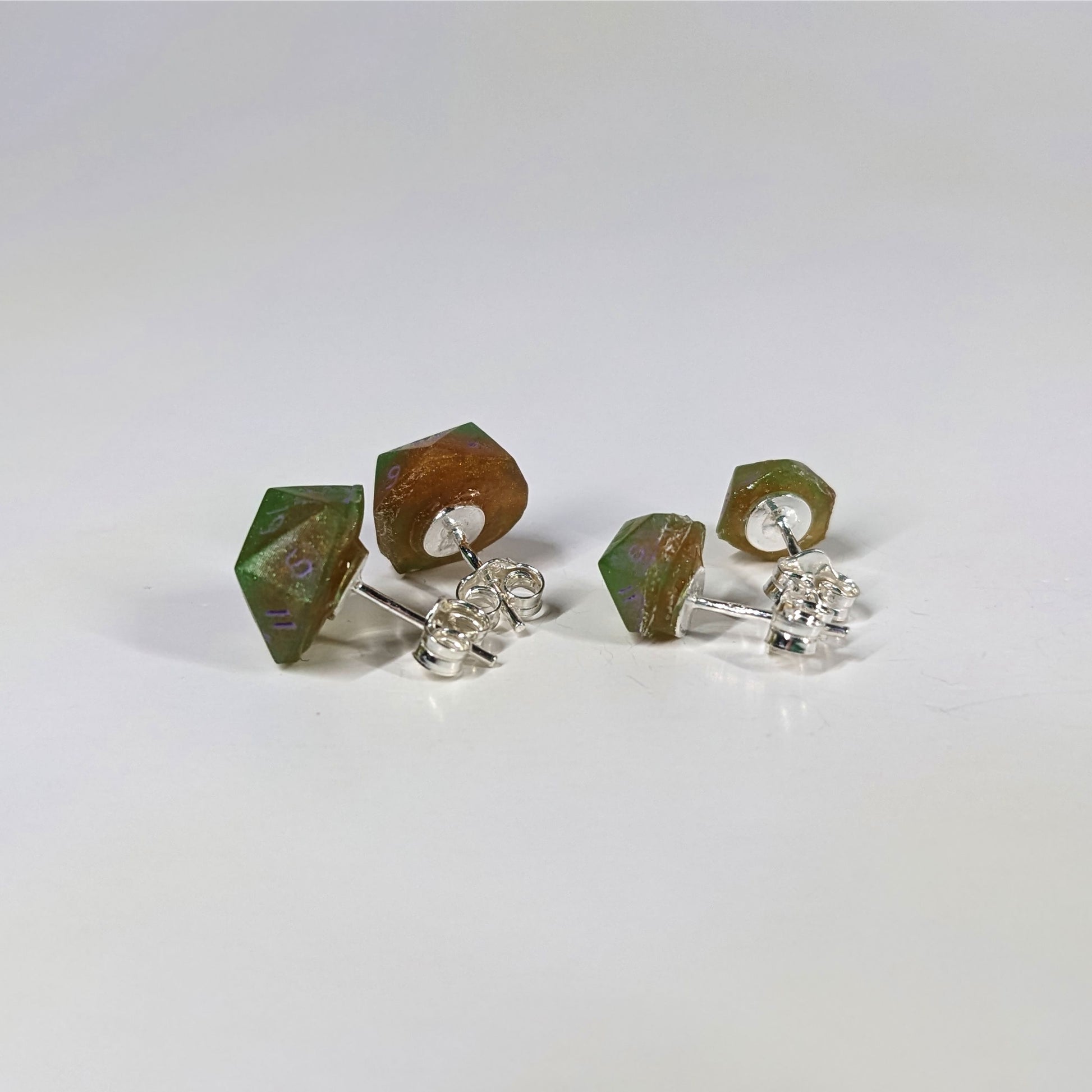 Two pairs of handmade d20 earrings that are bright green and red gold with purple numbers turned to show the sterling silver hardware and butterfly backs.