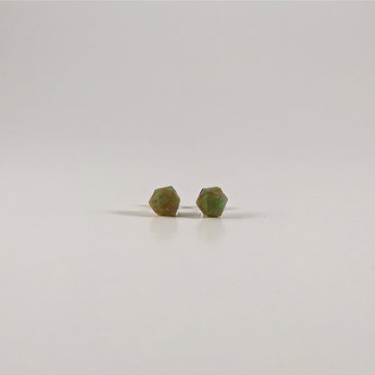 A single pair of the smaller size handmade d20 earrings with sterling silver hardware that are bright green and red gold with purple numbers on a white background. The earring on the left centers the 20 face and the earring on the right centers the 1 face.