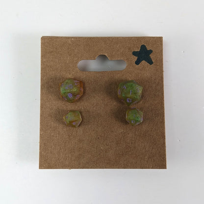 Two pairs of handmade d20 earrings with sterling silver hardware that are bright green and red gold with purple numbers on a kraft brown earring card with a star in the top right corner. The earrings on the left of each pair centers the 20 face and the earrings on the right of each pair centers the 1 face.