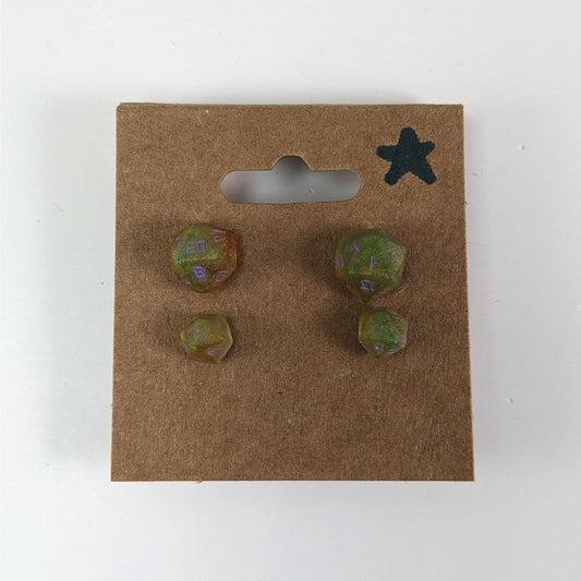 Two pairs of handmade d20 earrings with sterling silver hardware that are bright green and red gold with purple numbers on a kraft brown earring card with a star in the top right corner. The earrings on the left of each pair centers the 20 face and the earrings on the right of each pair centers the 1 face.