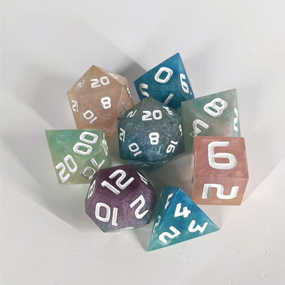A complete set of 8 handmade artisan dice that have swirls of translucent pink, purple, green, blue, and white with opaque white numbers. The DnD dice set is arranged in a circle and features 2 D20s, one of which is in the center surrounded by the other 7 dice on a white background.