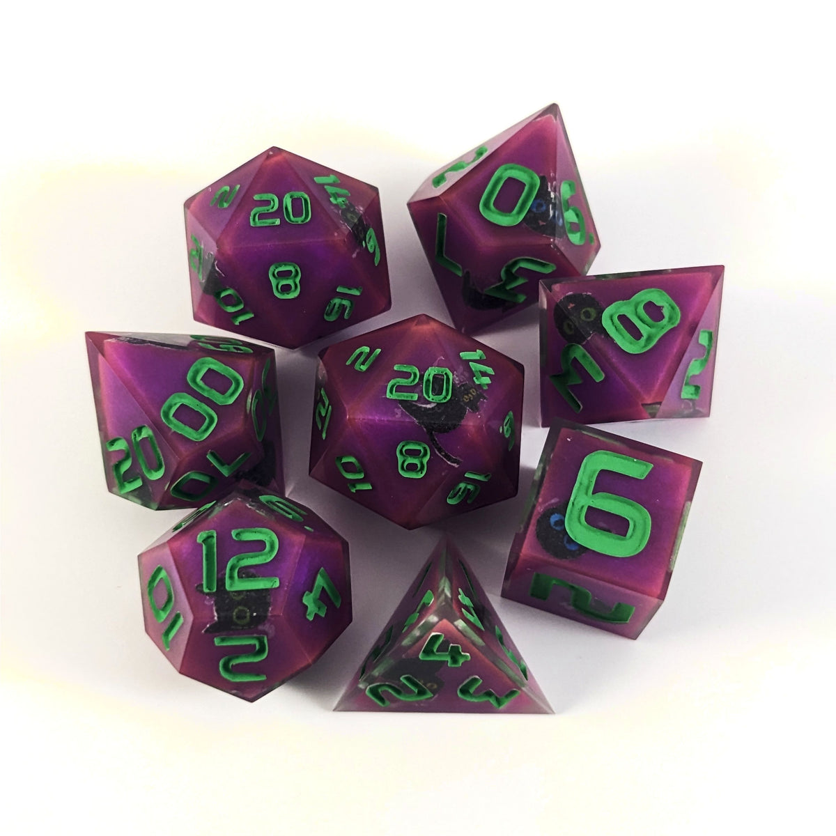 A complete set of 8 handmade artisan dice that are purple with black cat designs with bright green numbers. The DnD dice set is arranged in a circle and features 2 D20s, one of which is in the center surrounded by the other 7 dice on a white background.