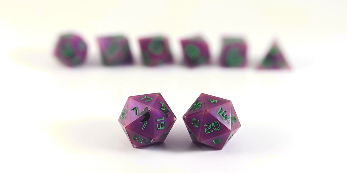 A straight on photo of a standard set of DnD dice that are purple with black cat designs with bright green numbers focusing on 2 d20s in the center. The d20 on the left has the 1 face centered and the d20 on the right has the 20 face centered. The other 6 dice are lined up in the background but are out of focus, while the d20s are in sharp focus.