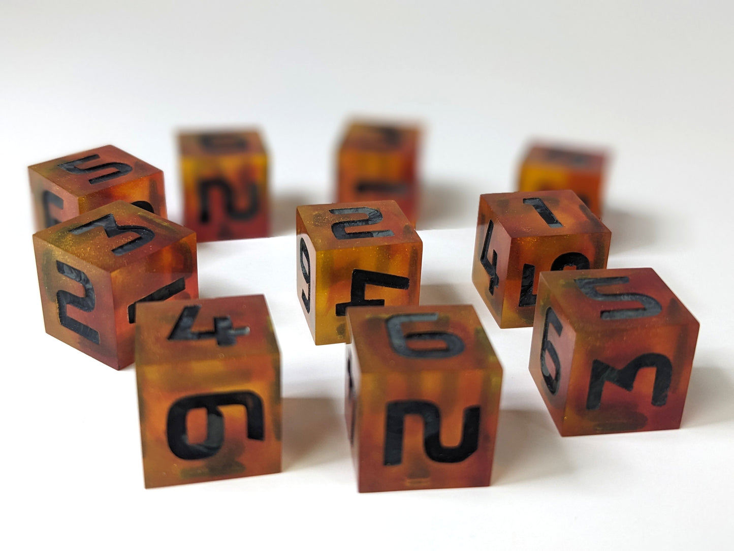 A low angle of 10 red and orange d6s with black and gray numbers. The dice in front are in sharp focus showing the swirls of orange with red while the dice in the back are blurred.