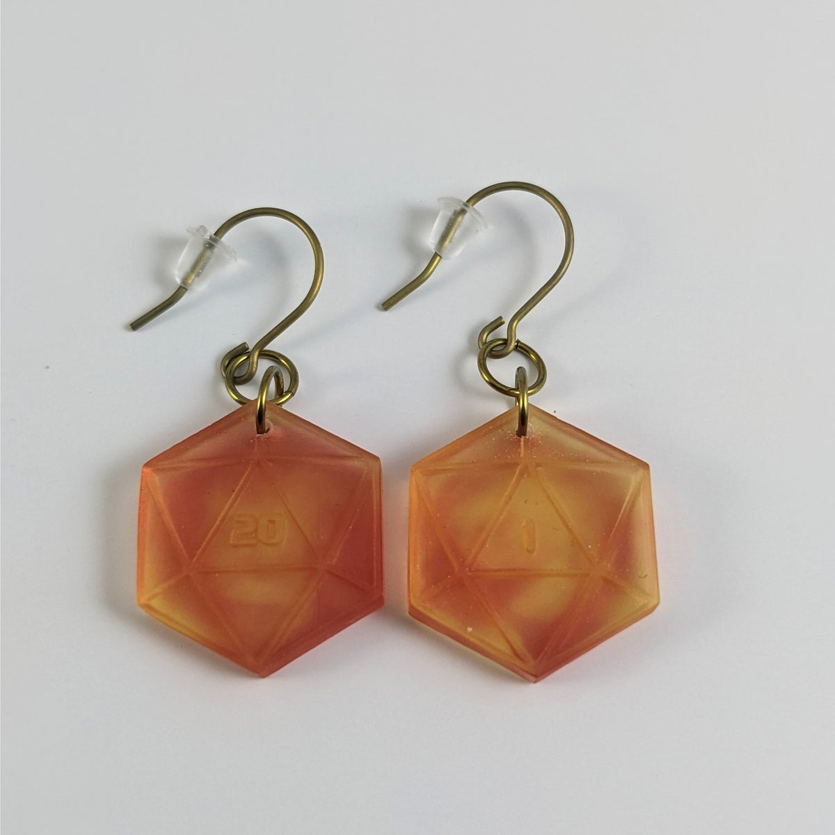 A pair of fiery red and orange dangly, flat d20 earrings with gold color titanium and niobium hardware and bell shaped rubber backs on a white background. The earring on the left has a 20 on it and the earring on the right has a 1 on it, both in a sci-fi style font.