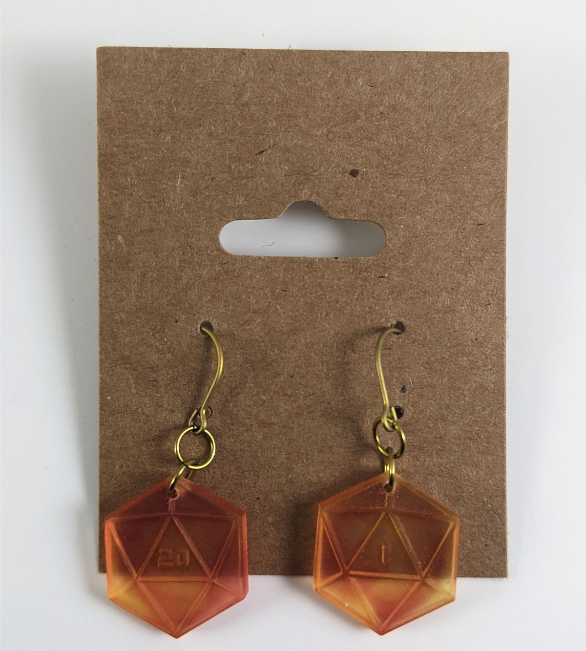 A pair of fiery red and orange dangly, flat d20 earrings with gold color titanium and niobium hardware on a kraft earring card on a white background. The earring on the left has a 20 on it and the earring on the right has a 1 on it, both in a sci-fi style font.