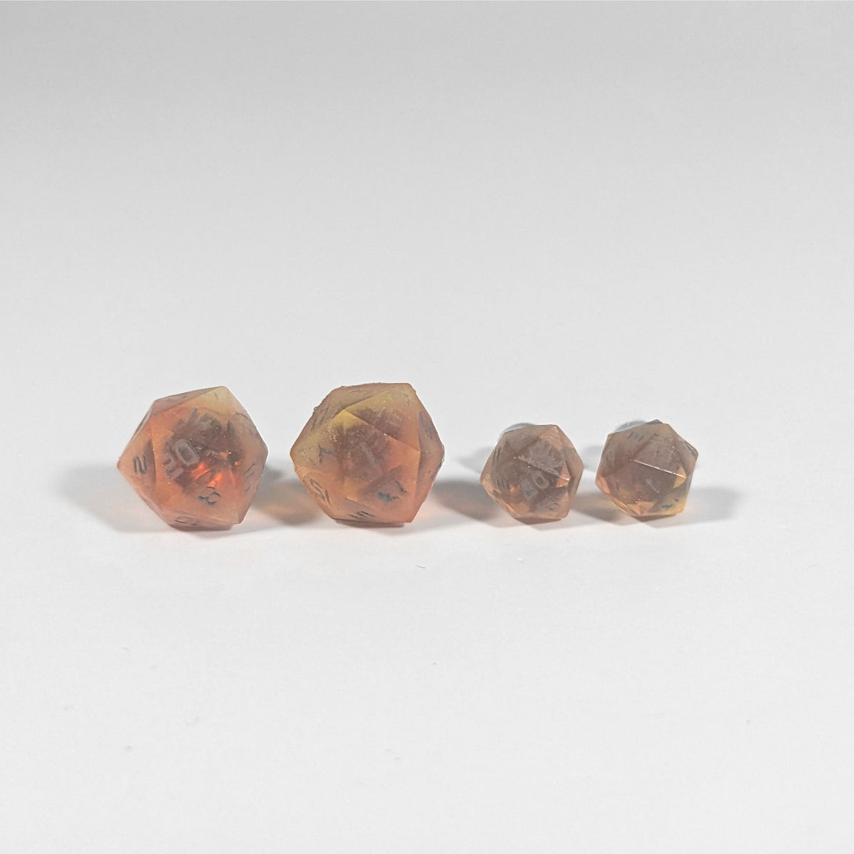 Two pairs of handmade d20 earrings with titanium hardware that are red and orange swirls with smokey gray numbers on a white background sit in a line with the larger pair on the left and the smaller pair on the right. The earrings on the left of each pair centers the 20 face and the earrings on the right of each pair centers the 1 face.