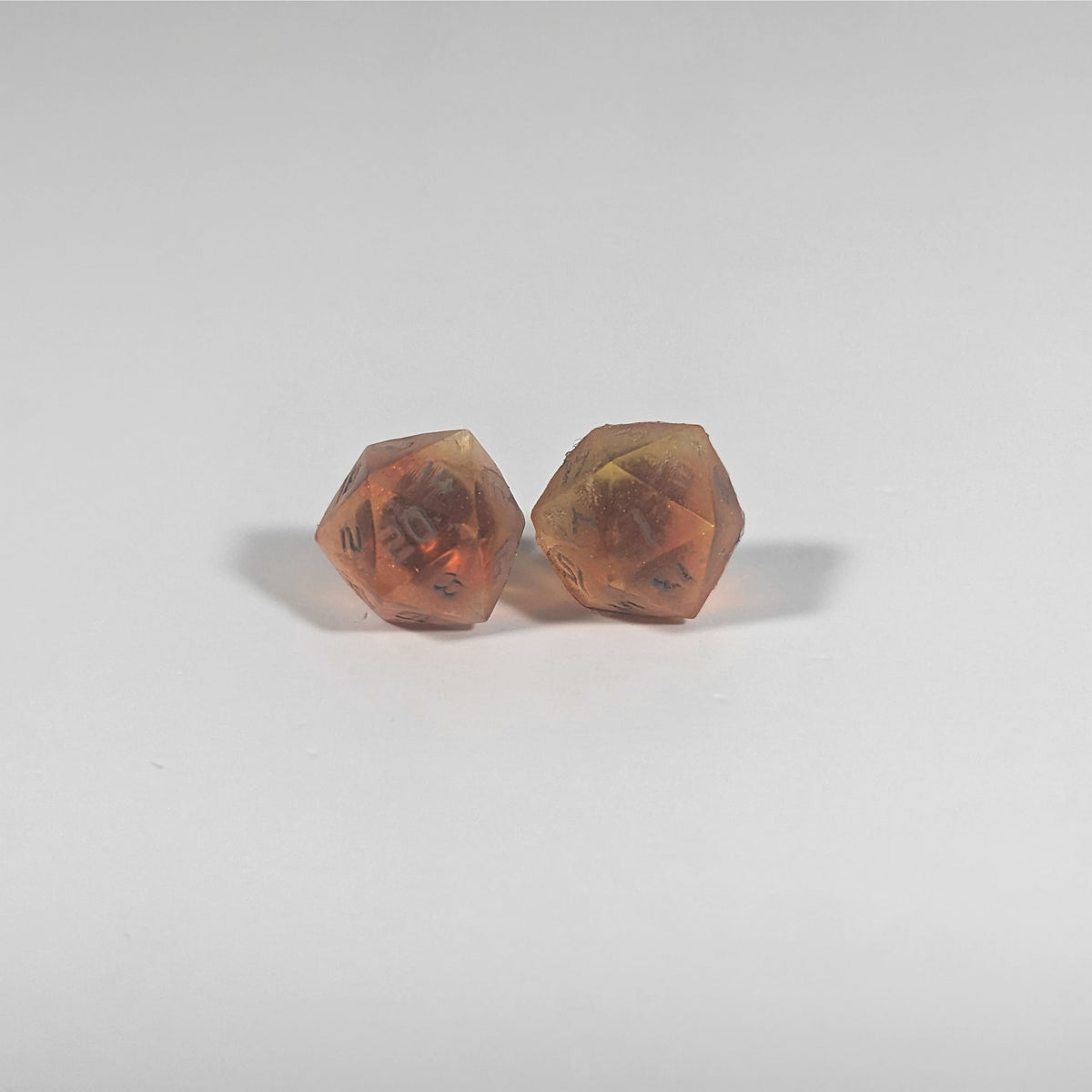 A single pair of the larger size handmade d20 earrings with titanium hardware that are red and orange swirls with smokey gray numbers on a white background. The earring on the left centers the 20 face and the earring on the right centers the 1 face.