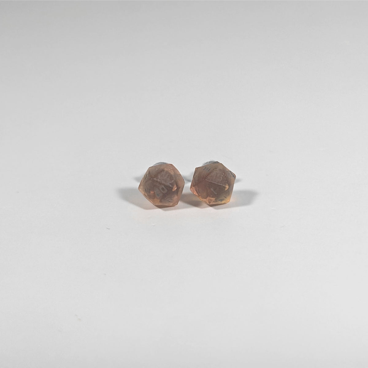 A single pair of the smaller size handmade d20 earrings with titanium hardware that are red and orange swirls with smokey gray numbers on a white background. The earring on the left centers the 20 face and the earring on the right centers the 1 face.