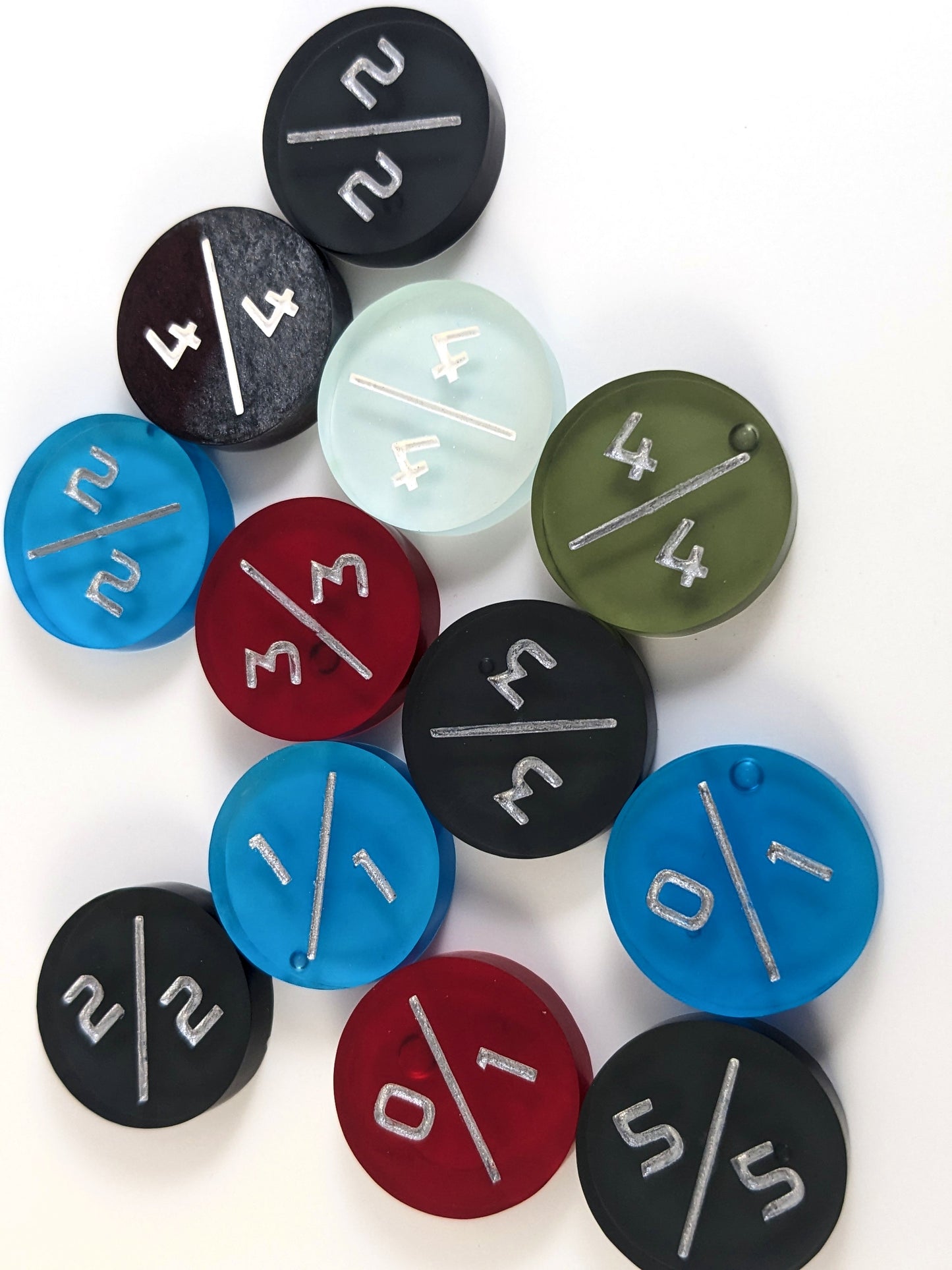 A collection of tokens which have minor cosmetic flaws in a variety of colors and power toughness numbers on a white background. Each token is face up, and some of the bubbles on the back of the tokens are visible.