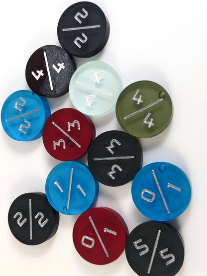A collection of tokens which have minor cosmetic flaws in a variety of colors and power toughness numbers on a white background. Each token is face up, and some of the bubbles on the back of the tokens are visible.