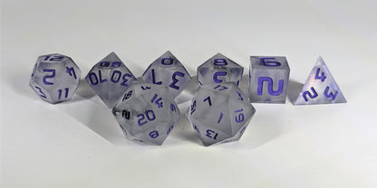 A straight on photo of a standard set of DnD dice that have black swirls around a cloudy insert and purple numbers focusing on 2 d20s in the center. The d20 on the left has the 20 face centered and the d20 on the right has the 1 face centered. The other 6 dice are lined up in the background.