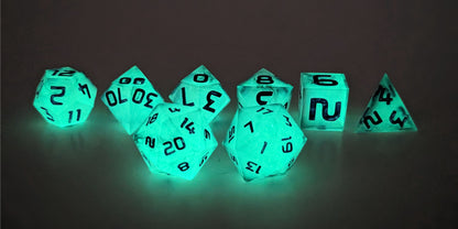 A straight on photo of a standard set of DnD dice that have black swirls showing through glow-in-the-dark green inserts and purple numbers focusing on 2 d20s in the center. The d20 on the left has the 20 face centered and the d20 on the right has the 1 face centered. The other 6 dice are lined up in the background.