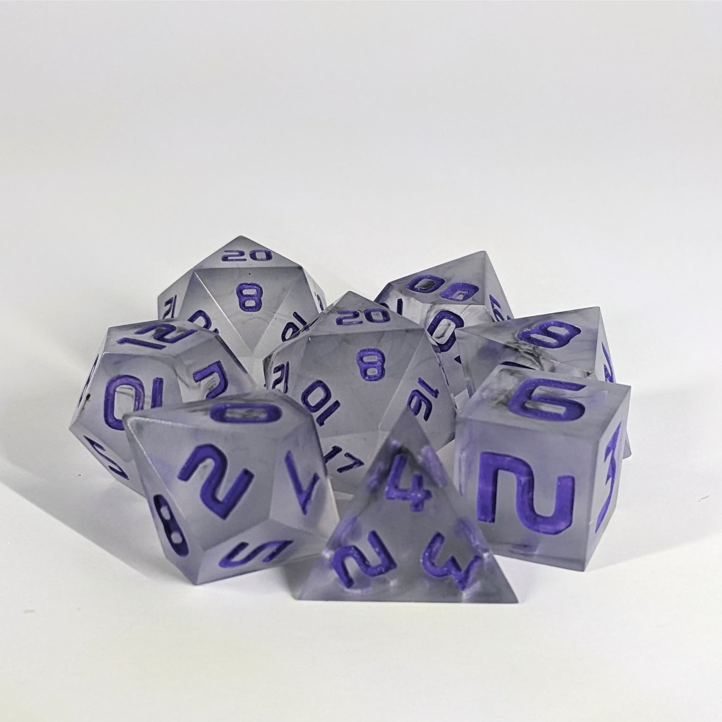 A complete set of 8 handmade artisan dice that have black swirls around a cloudy insert with purple numbers. The DnD dice set is arranged in a circle and features 2 D20s, one of which is in the center surrounded by the other 7 dice.