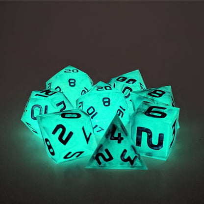 A complete set of 8 polyhedral dice that with inserts glowing green, black swirls and purple numbers, showing the glow-in-the-dark feature of this dice set. The DnD dice set is arranged in a circle and features 2 D20s, one of which is in the center surrounded by the other 7 dice.