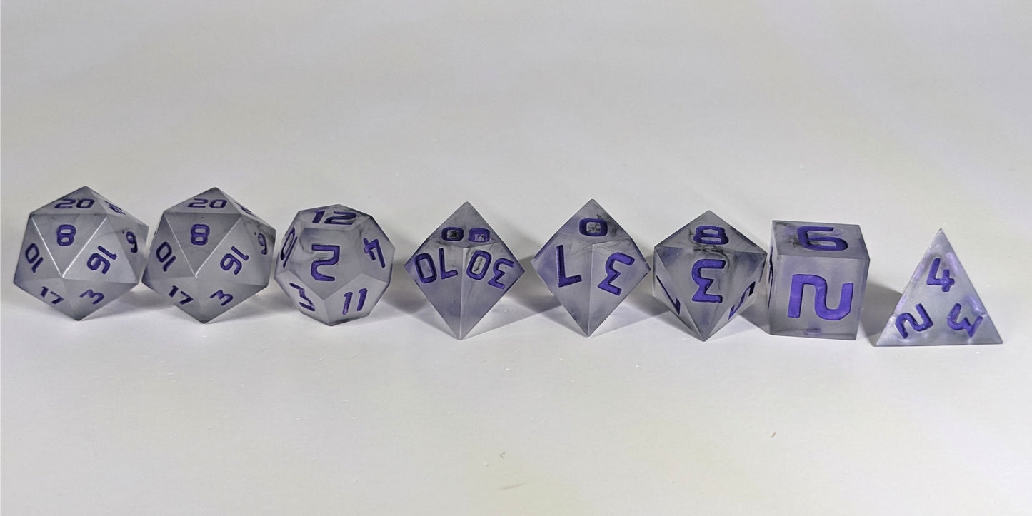 A straight on photo of a complete set of polyhedral dice that have black swirls around a cloudy insert and purple numbers arranged in a straight line. They are lined up with the 2 d20s on the left going down to the d4 on the right side. The highest value number of each die is facing up.