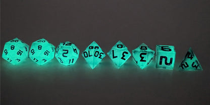A straight on photo of a complete set of polyhedral dice that have glowing green inserts and have purple numbers arranged in a straight line. They are lined up with the 2 d20s on the left going down to the d4 on the right side. The highest value number of each die is facing up. This image shows the glow-in-the-dark feature of this dice set and that you can still see the black swirls through the glow.