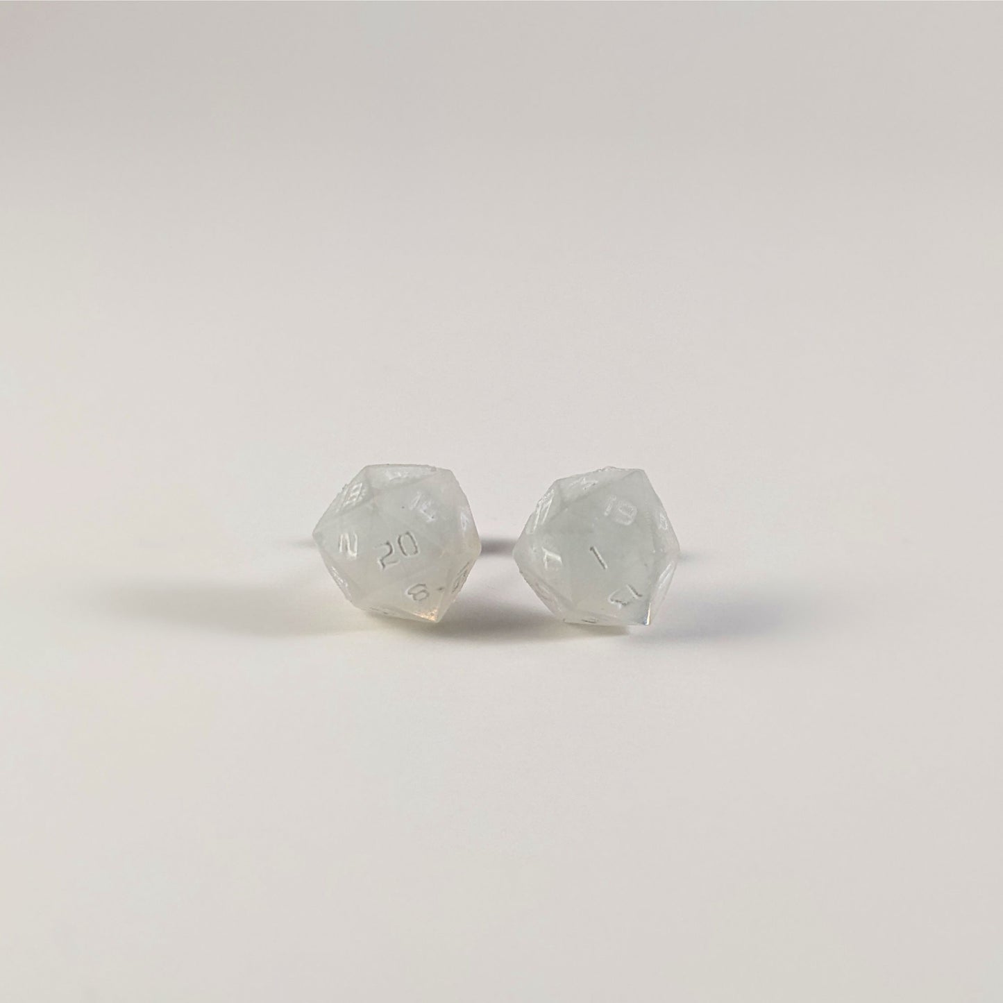 A single pair of the larger size handmade d20 earrings that are frosty white with white numbers on a white background. The earring on the left centers the 20 face and the earring on the right centers the 1 face.