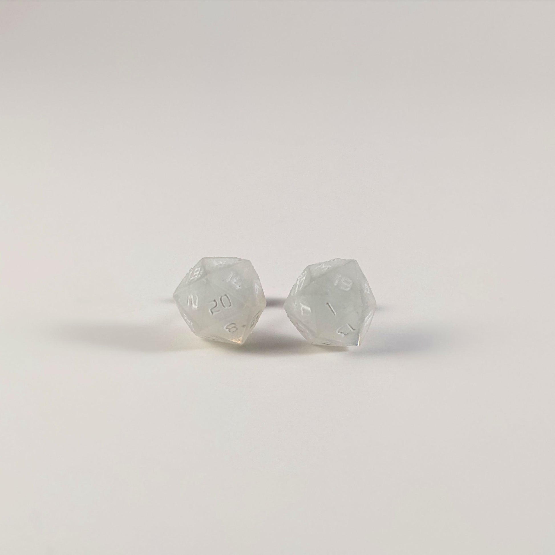 A single pair of the larger size handmade d20 earrings that are frosty white with white numbers on a white background. The earring on the left centers the 20 face and the earring on the right centers the 1 face.