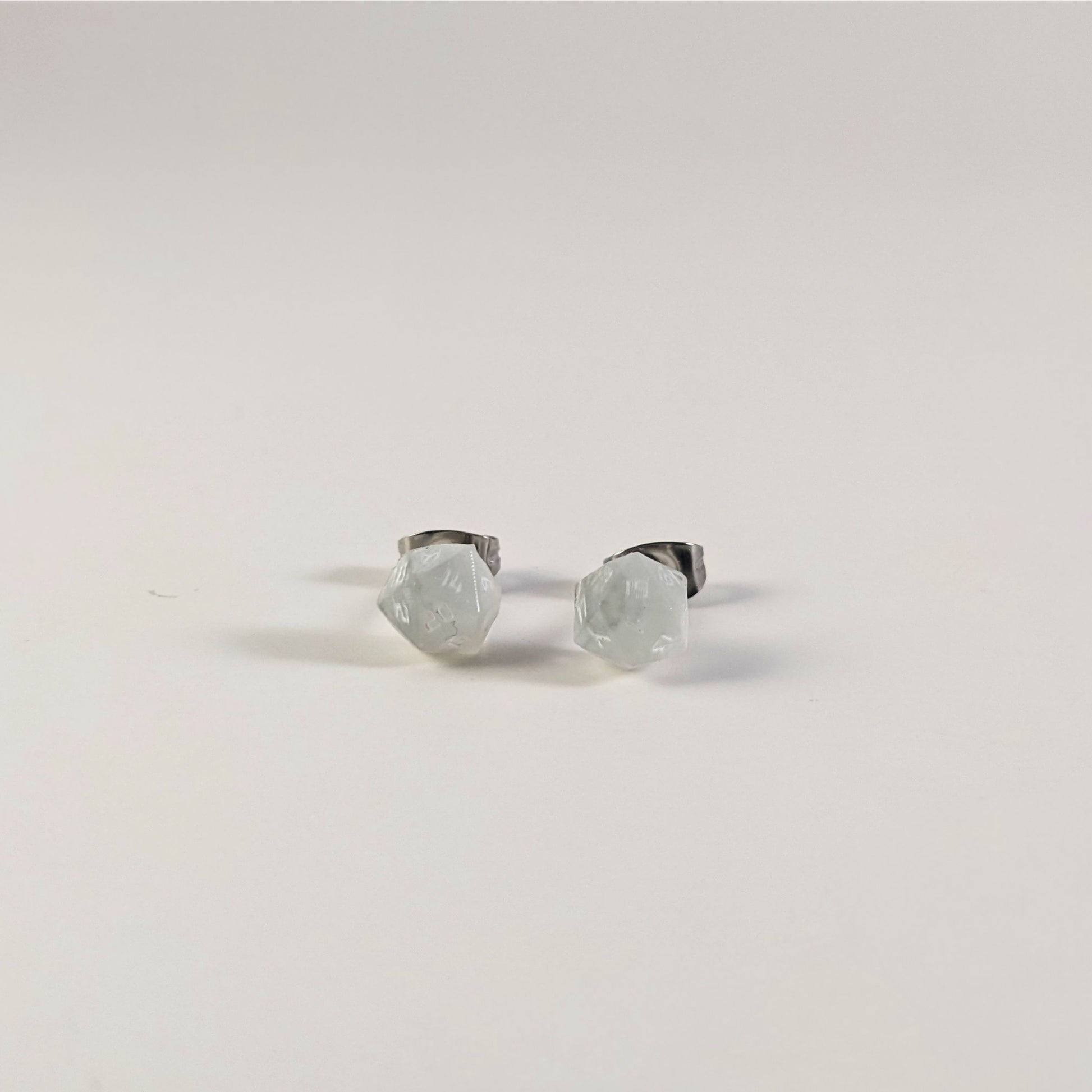 A single pair of the smaller size handmade d20 earrings that are frosty white with white numbers on a white background. The earring on the left centers the 20 face and the earring on the right centers the 1 face.