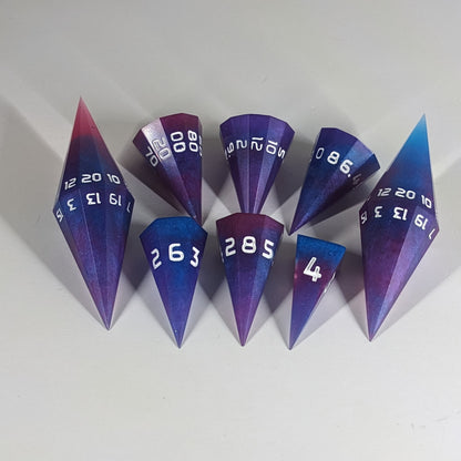 The dagger style DnD dice set that is purple, pink, and blue galaxy swirls with an extra touch of glitter and white numbers is arranged with a d20 each on the right and left, with the d%, d12, and d10 along the top and the d6, d8, and d4 along the bottom, all in line with the d20.