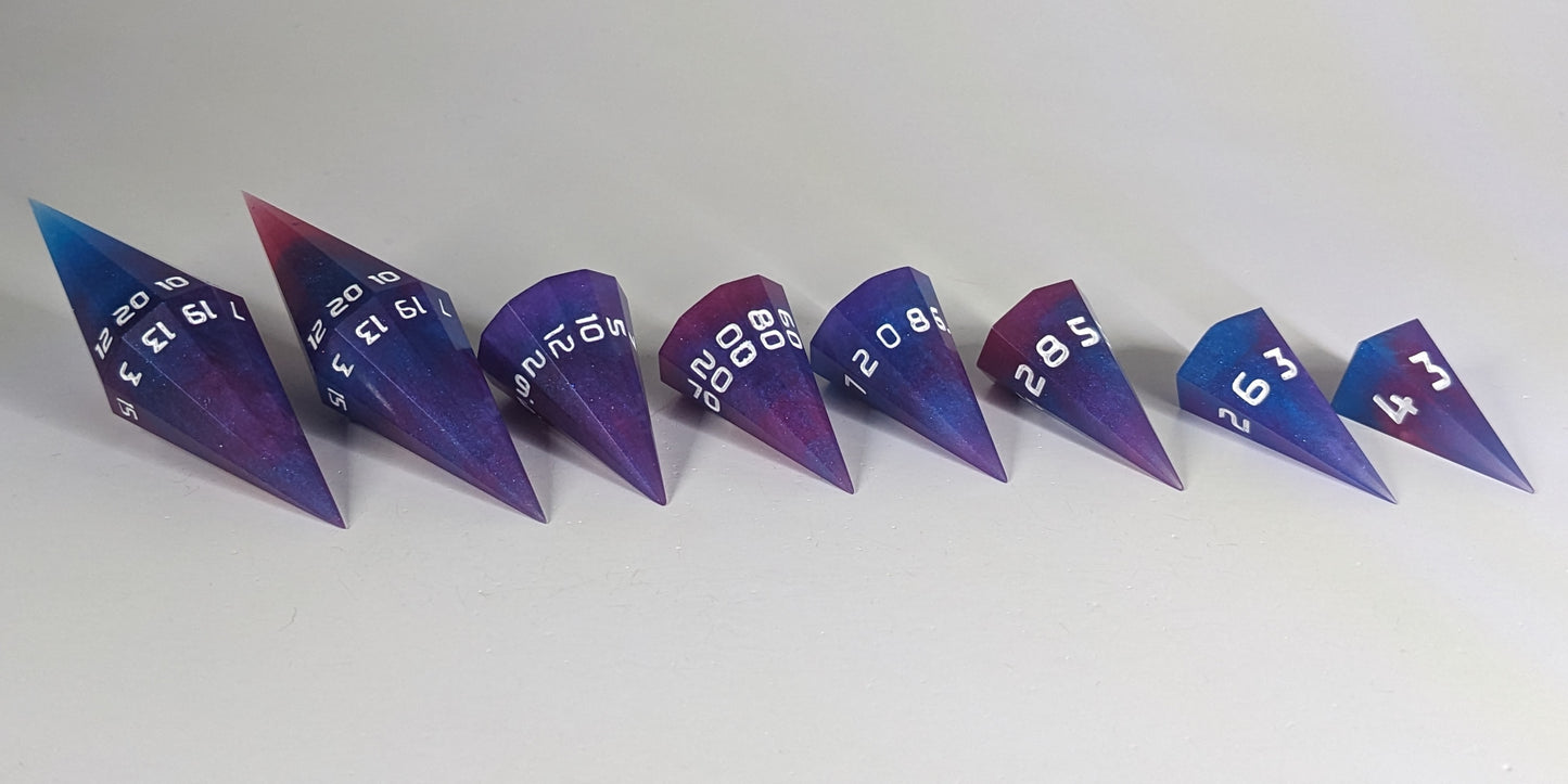 A straight on photo of a complete set of dagger DnD dice that are purple, pink, and blue galaxy swirls with an extra touch of glitter and white numbers arranged in a straight line with points angled toward the right. They are lined up with the 2 d20s on the left going down to the d4 on the right side. The highest value number of each die is facing forward.