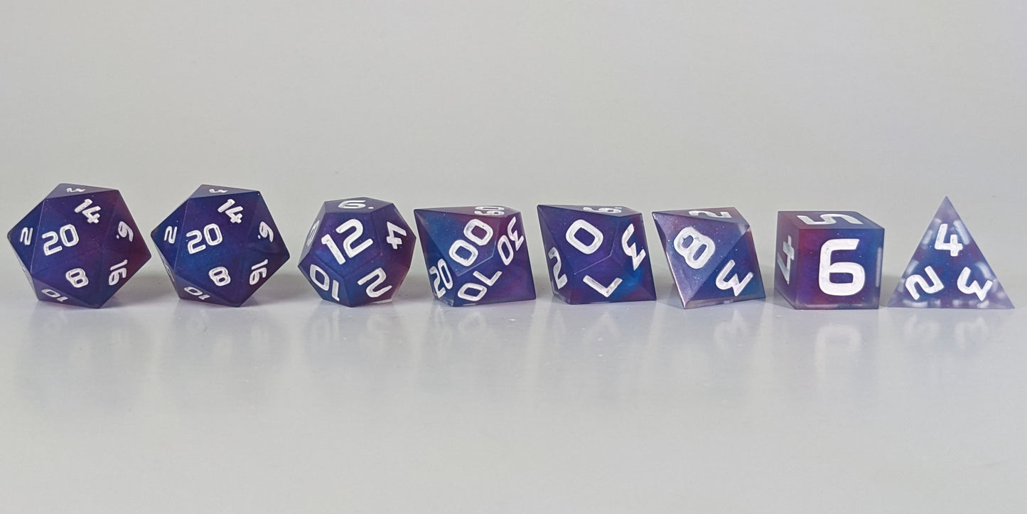 A straight on photo of a complete set of polyhedral dice that are purple, pink, and blue swirls with a clear shell with extra glitter and white numbers arranged in a straight line. They are lined up with the 2 d20s on the left going down to the d4 on the right side. The highest value number of each die is facing forward.