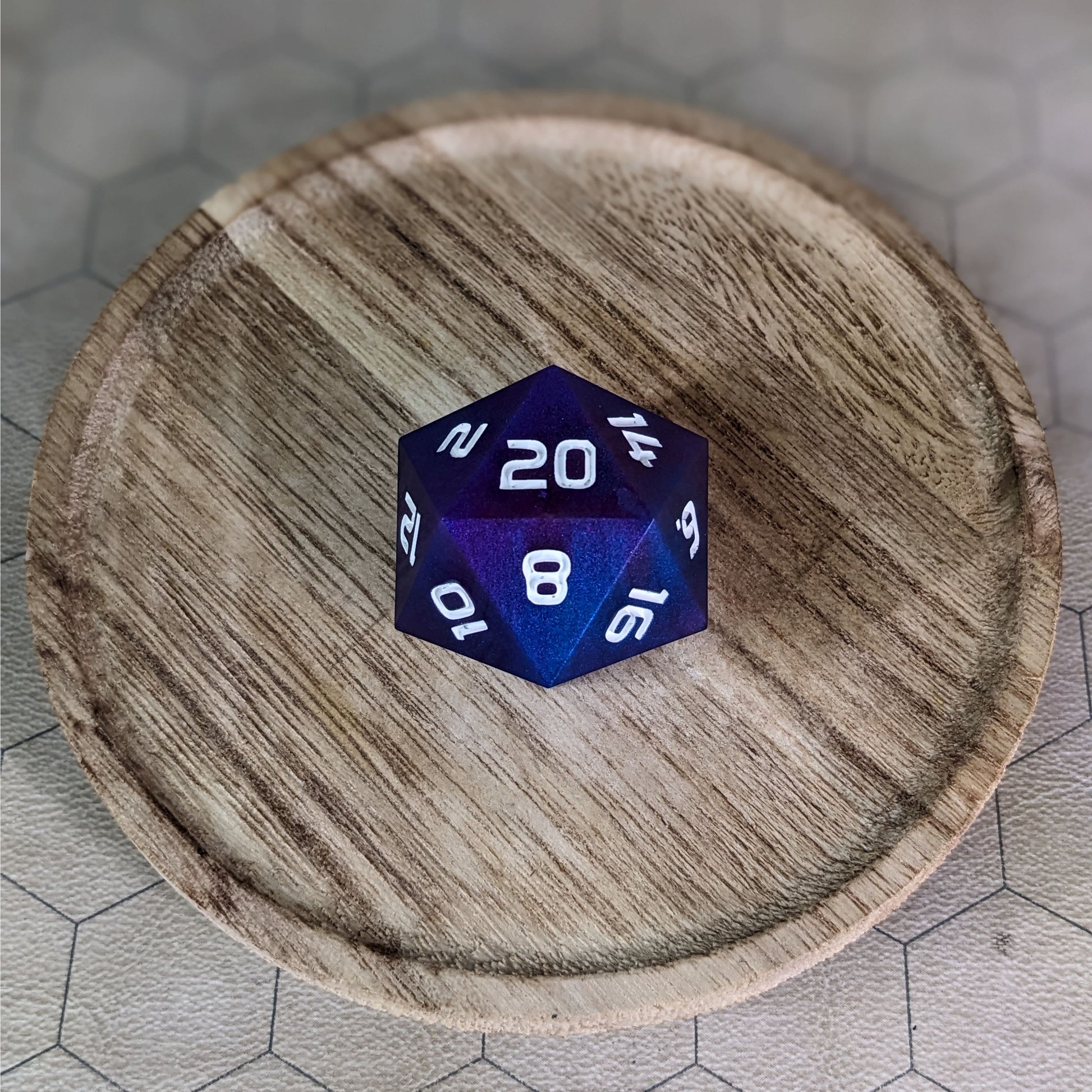 A high angle view of a large d20 with subtle swirls of purple, blue, and pink with white numbers. It is sitting in the center of a wooden circle.
