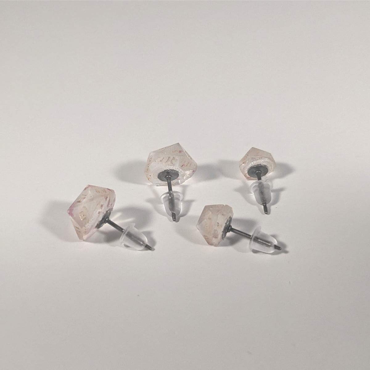 Two pairs of handmade d20 earrings that are glittery clear with pink flakies with gold numbers turned to show the titanium hardware and bell shaped rubber backs.