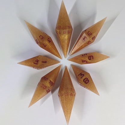 A complete set of resin dice featuring 2 d20s for advantage rolls. These shimmering gold and red gold swirls and red numbering slender handmade diamond dice are clustered in a tight circle on a white background, highlighting the quality of the artisan dice craftsmanship and the unique pointed shape.
