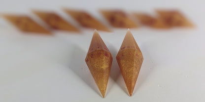 A stylized macro shot focusing heavily on 2 d20s from a shimmering gold and red gold swirls and red numbering handmade dice set in the foreground. The sharp diamond edges of these front resin dice are crisp, while the rest of the matching artisan dice collection forms a softly blurred background, creating depth.