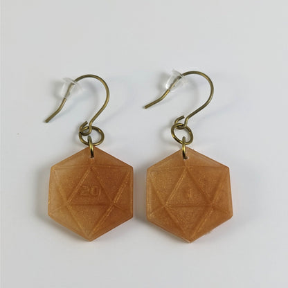 A pair of sparkling gold dangly, flat d20 earrings with gold color titanium and niobium hardware and bell shaped rubber backs on a white background. The earring on the left has a 20 on it and the earring on the right has a 1 on it, both in a sci-fi style font.