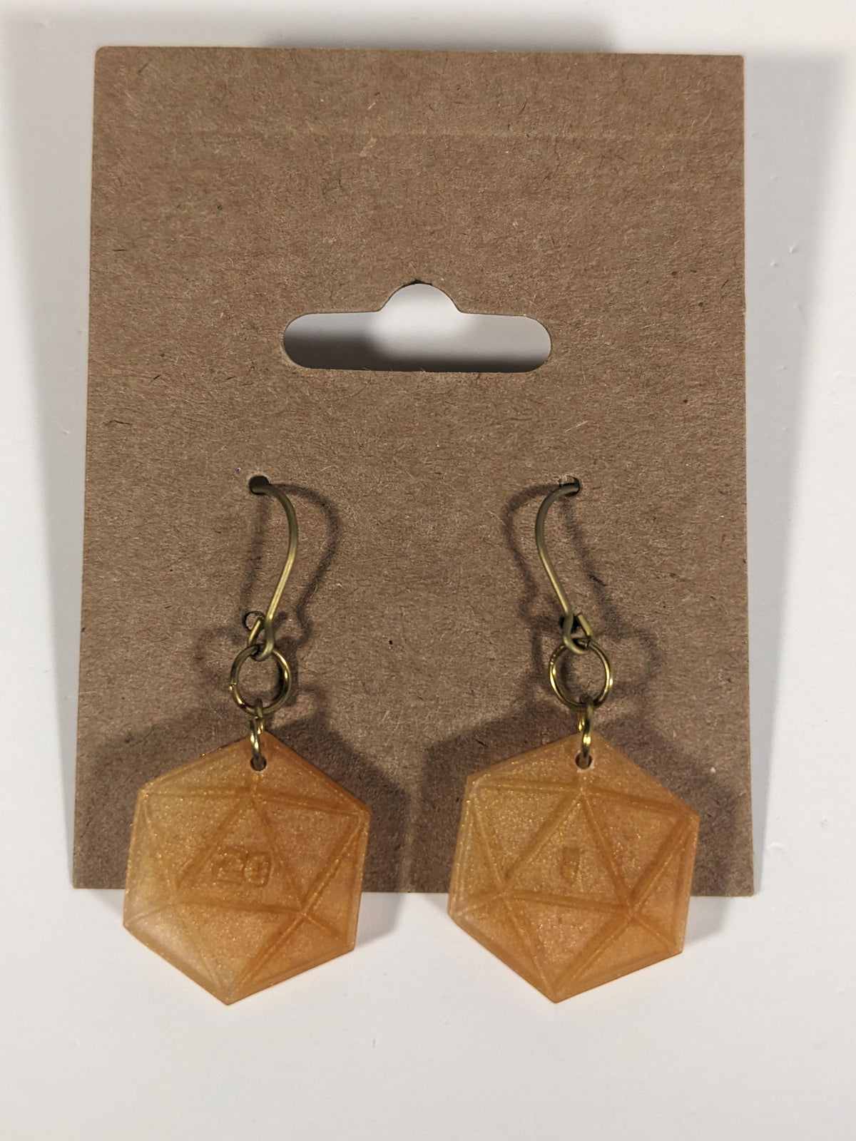 A pair of sparkly gold dangly, flat d20 earrings with gold color titanium and niobium hardware on a kraft earring card on a white background. The earring on the left has a 20 on it and the earring on the right has a 1 on it, both in a sci-fi style font.