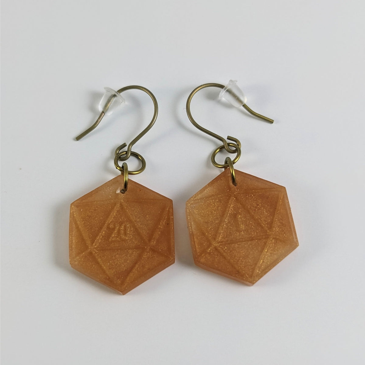 A pair of sparkly gold dangly, flat d20 earrings with gold color titanium and niobium hardware and bell shaped rubber backs on a white background. The earring on the left has a 20 on it and the earring on the right has a 1 on it, both in a fantasy style font.