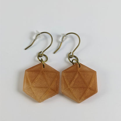 A pair of sparkly gold dangly, flat d20 earrings with gold color titanium and niobium hardware and bell shaped rubber backs on a white background.