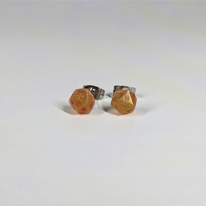 A single pair of the smaller size handmade d20 earrings that are shimmering gold with red numbers on a white background. The earring on the left centers the 20 face and the earring on the right centers the 1 face.