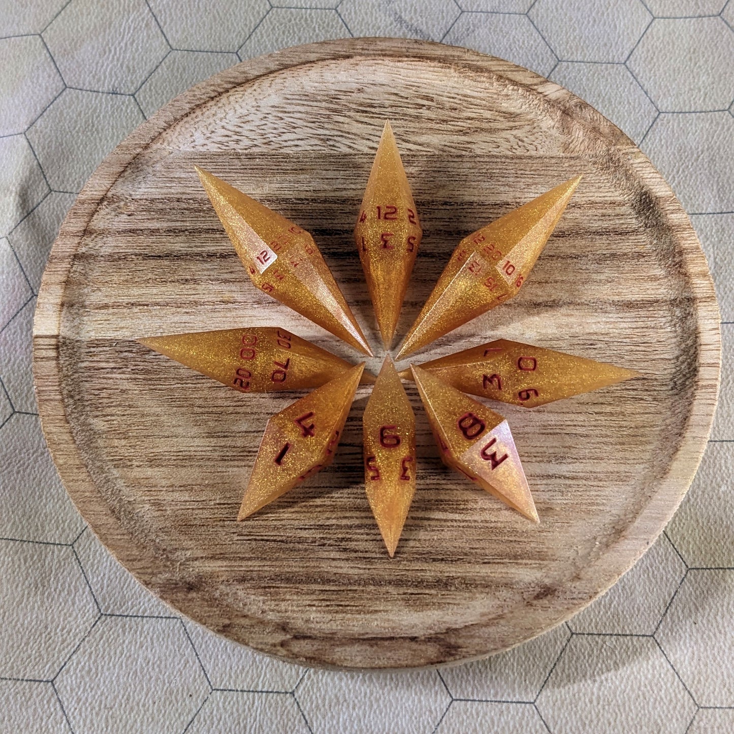A set of shimmering gold and red gold swirls and red numbering handmade dice arranged on a wooden circle. The resin dice feature a unique pointed diamond shape with the tips facing outward, and the highest number of each die is facing up.