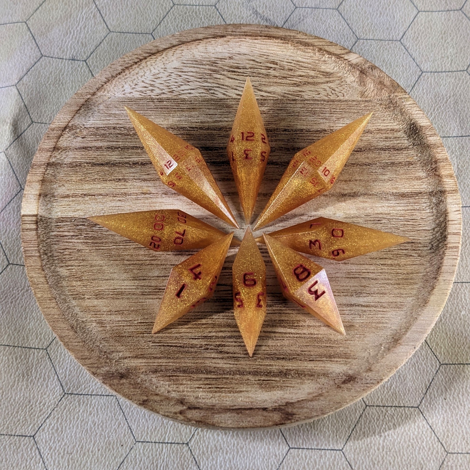A set of shimmering gold and red gold swirls and red numbering handmade dice arranged on a wooden circle. The resin dice feature a unique pointed diamond shape with the tips facing outward, and the highest number of each die is facing up.