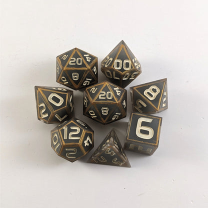 A complete set of 8 handmade artisan dice that are gray with subtle marbling with painted gold lines along the edges a clear shell with ivory numbers. The DnD dice set is arranged in a circle and features 2 D20s, one of which is in the center surrounded by the other 7 dice.