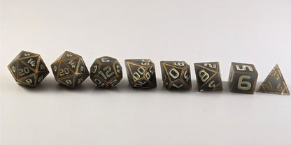 A straight on photo of a complete set of polyhedral dice that are gray with subtle marbling with painted gold lines along the edges a clear shell with ivory numbers arranged in a straight line. They are lined up with the 2 d20s on the left going down to the d4 on the right side. The highest value number of each die is facing forward.