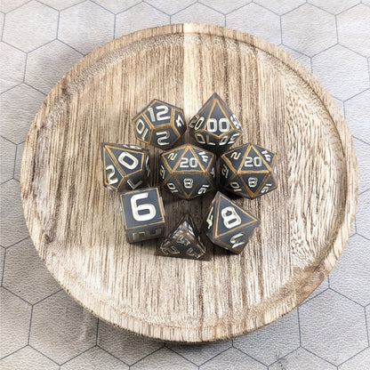 A complete set of 8 handmade artisan dice that are gray with subtle marbling with painted gold lines along the edges in a clear shell with ivory numbers. The DnD dice set is on a wooden circle and the dice are arranged in a circle and features 2 D20s, one of which is in the center surrounded by the other 7 dice.