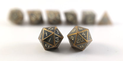 A straight on photo of a standard set of dice that are gray with subtle marbling with painted gold lines along the edges a clear shell with ivory numbers focusing on 2 d20s in the center. The d20 on the left has the 1 face centered and the d20 on the right has the 20 face centered. The other 6 dice are lined up in the background but are out of focus, while the d20s are in sharp focus.