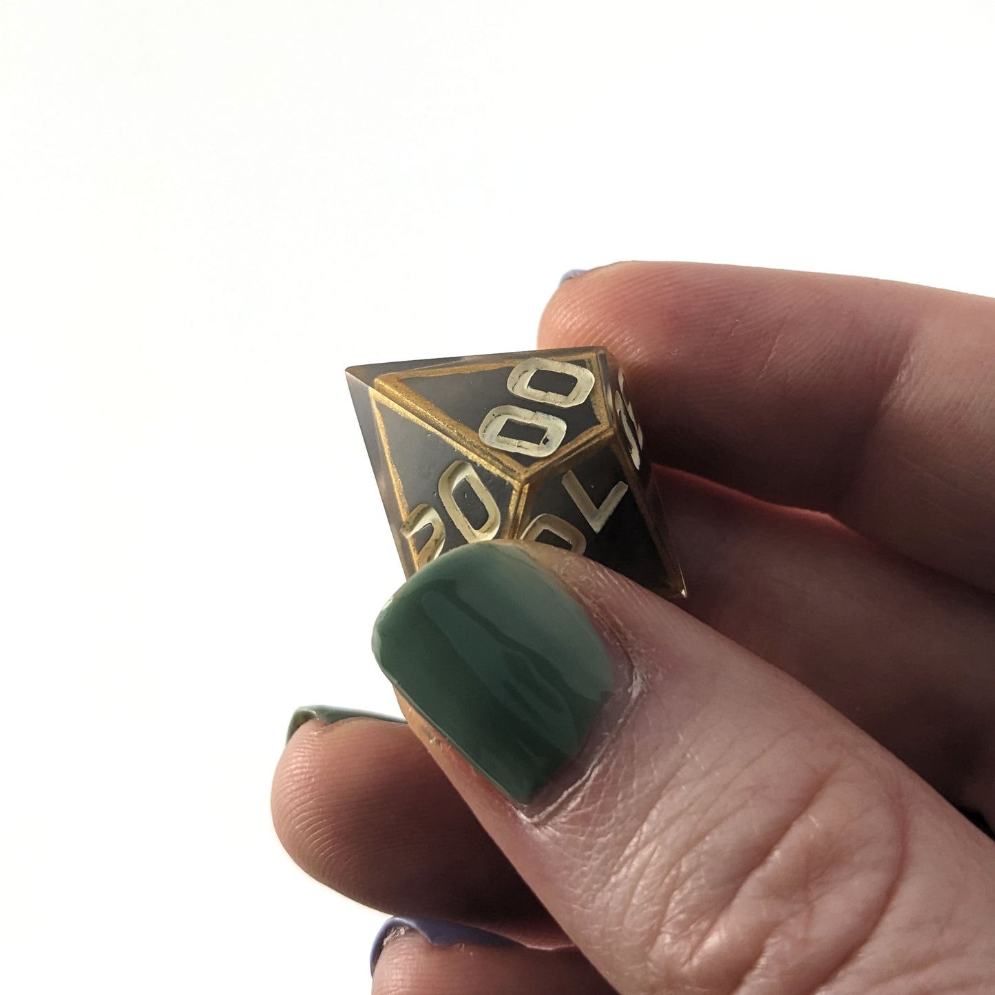 The d% that is gray with subtle marbling with painted gold lines along the edges a clear shell with ivory is held up to the camera at an angle to show the 00 face. The first 0 has a minor cosmetic flaw in the middle of the first 0. The numbers are still clear and it would have no affect on rolling.