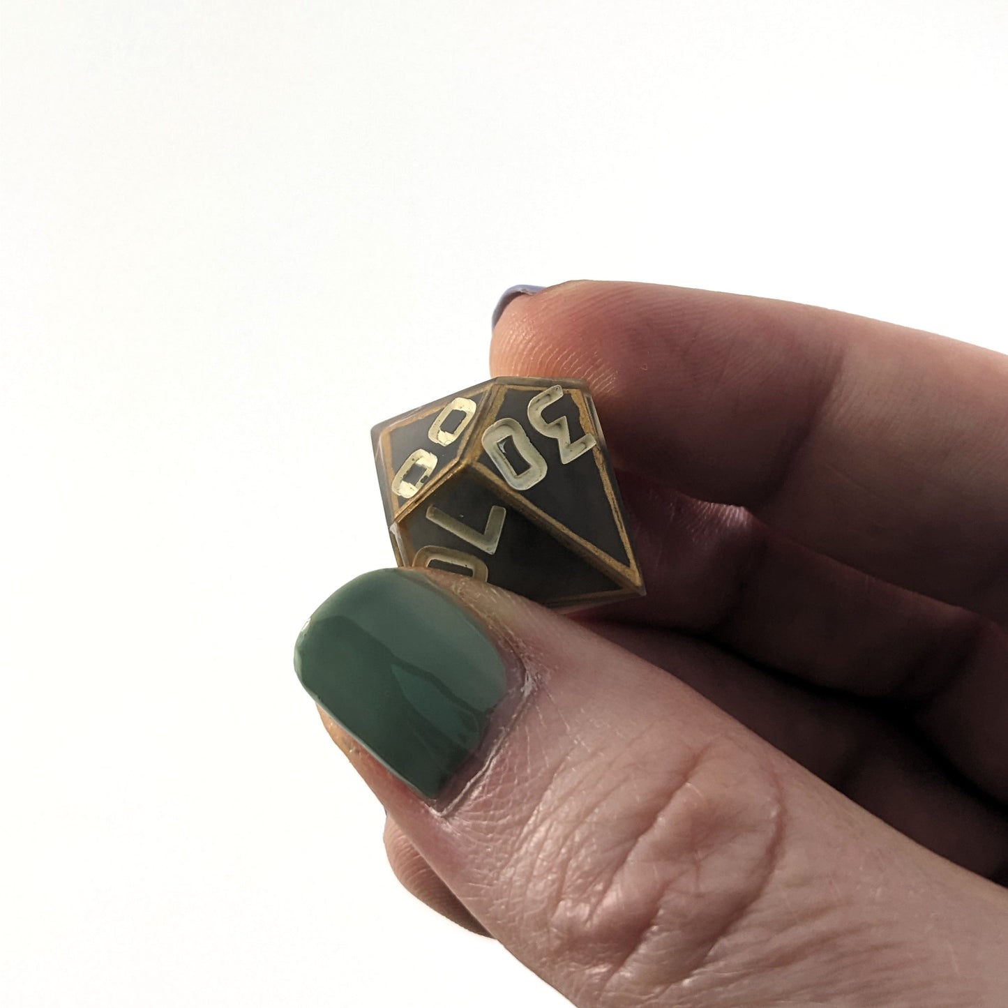 The d% that is gray with subtle marbling with painted gold lines along the edges a clear shell with ivory is held up to the camera at an angle to show the 30 face. The 0 has a minor cosmetic flaw in the middle. The numbers are still clear and it would have no affect on rolling. The 00 face is also visible with a similar flaw in the first 0 of that face.