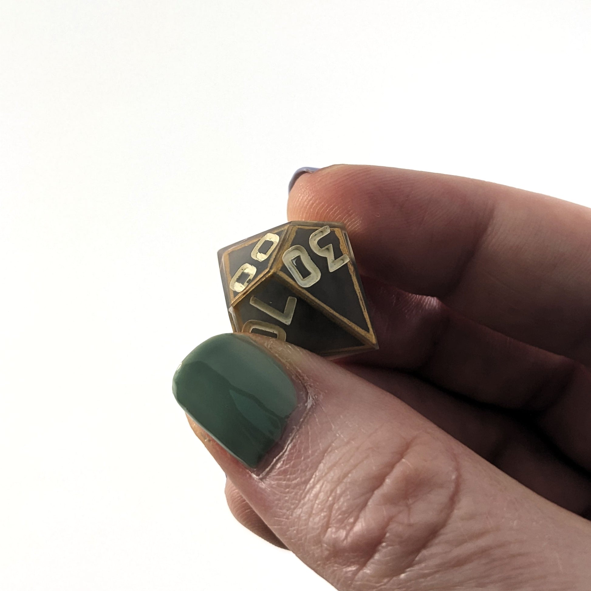 The d% that is gray with subtle marbling with painted gold lines along the edges a clear shell with ivory is held up to the camera at an angle to show the 30 face. The 0 has a minor cosmetic flaw in the middle. The numbers are still clear and it would have no affect on rolling. The 00 face is also visible with a similar flaw in the first 0 of that face.