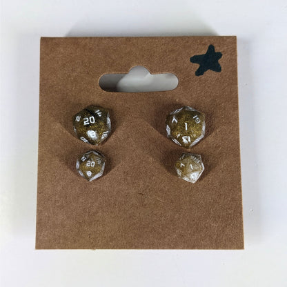 Two pairs of handmade d20 earrings with sterling silver hardware that are glittering gold and black with white numbers on a kraft brown earring card with a star in the top right corner. The earrings on the left of each pair centers the 20 face and the earrings on the right of each pair centers the 1 face.