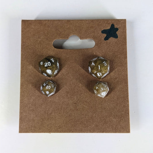 Two pairs of handmade d20 earrings with sterling silver hardware that are glittering gold and black with white numbers on a kraft brown earring card with a star in the top right corner. The earrings on the left of each pair centers the 20 face and the earrings on the right of each pair centers the 1 face.
