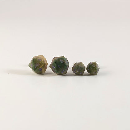 Two pairs of handmade d20 earrings with sterling silver hardware that are dark green and bright gold with purple numbers on a white background sit in a line with the larger pair on the left and the smaller pair on the right. The earrings on the left of each pair centers the 20 face and the earrings on the right of each pair centers the 1 face.