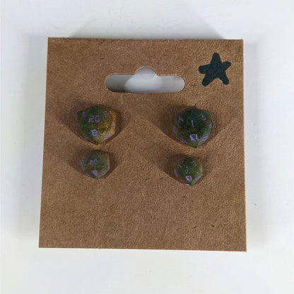 Two pairs of handmade d20 earrings with sterling silver hardware that are dark green and bright gold with purple numbers on a kraft brown earring card with a star in the top right corner. The earrings on the left of each pair centers the 20 face and the earrings on the right of each pair centers the 1 face.