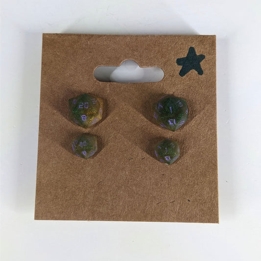 Two pairs of handmade d20 earrings with sterling silver hardware that are dark green and bright gold with purple numbers on a kraft brown earring card with a star in the top right corner. The earrings on the left of each pair centers the 20 face and the earrings on the right of each pair centers the 1 face.